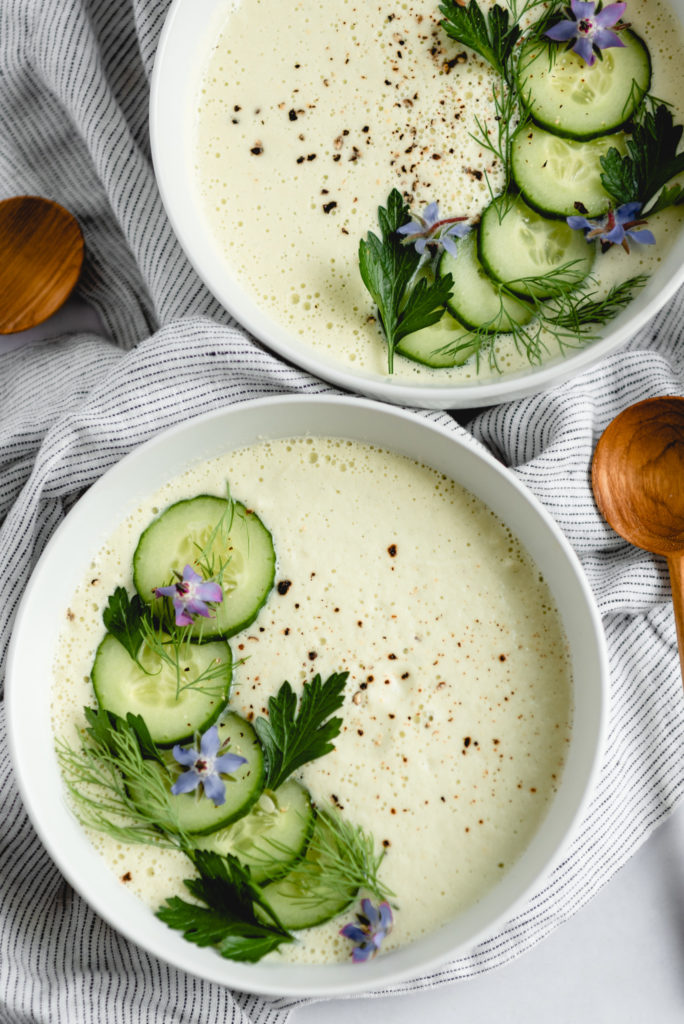 cucumber soup in white bowl with herbs and borage flowers