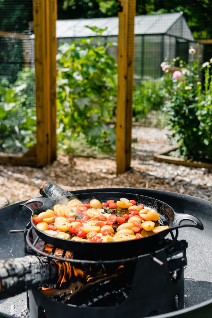 cherry tomatoes roasting on cast iron on open flame near garden