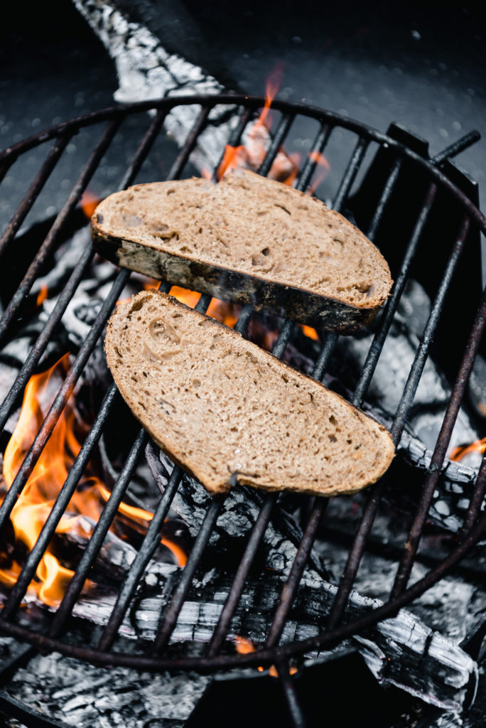two pieces of sourdough toasting on an open grill flame