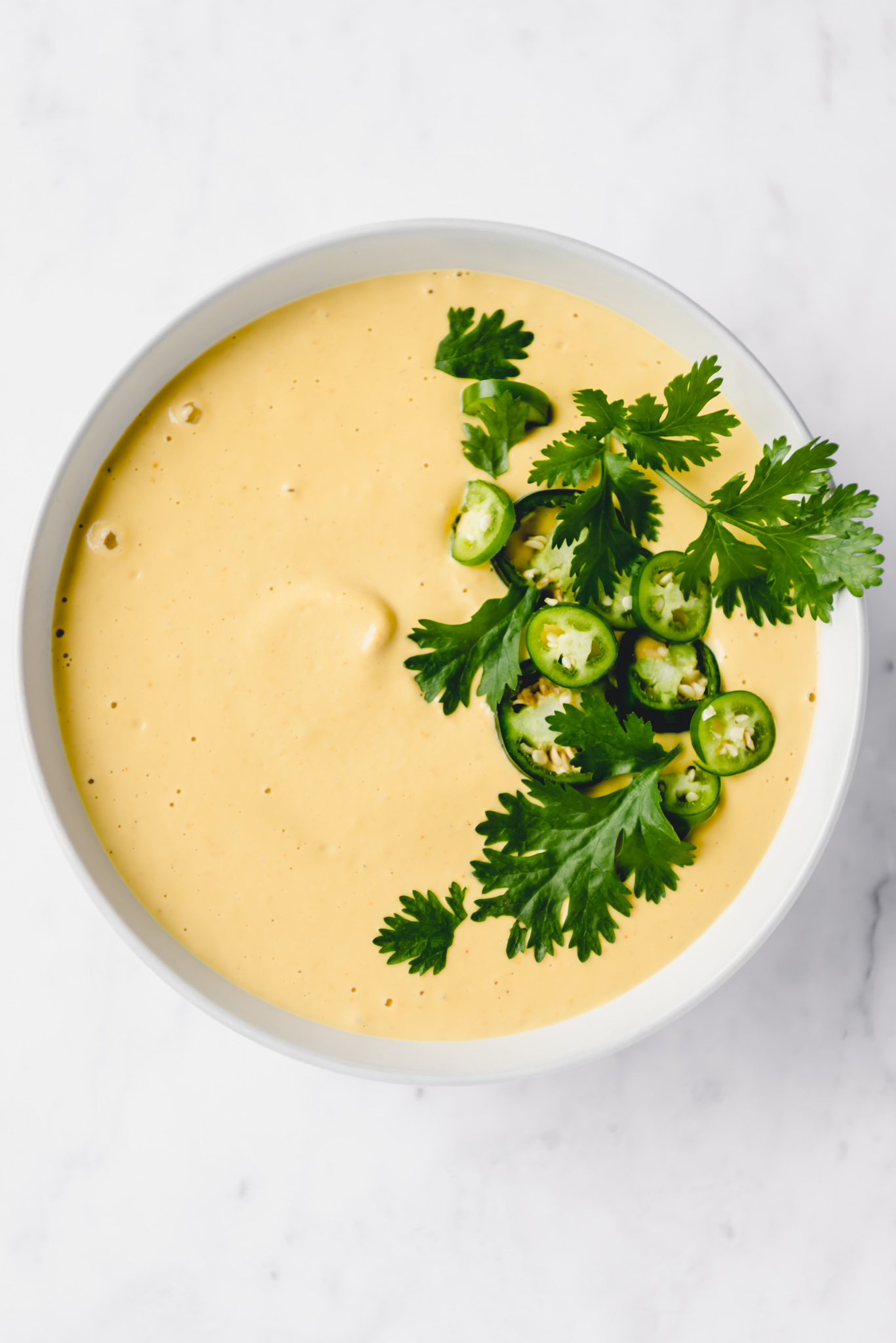 vegan nacho cheese bowl garnished with jalapeno and cilantro on a white background