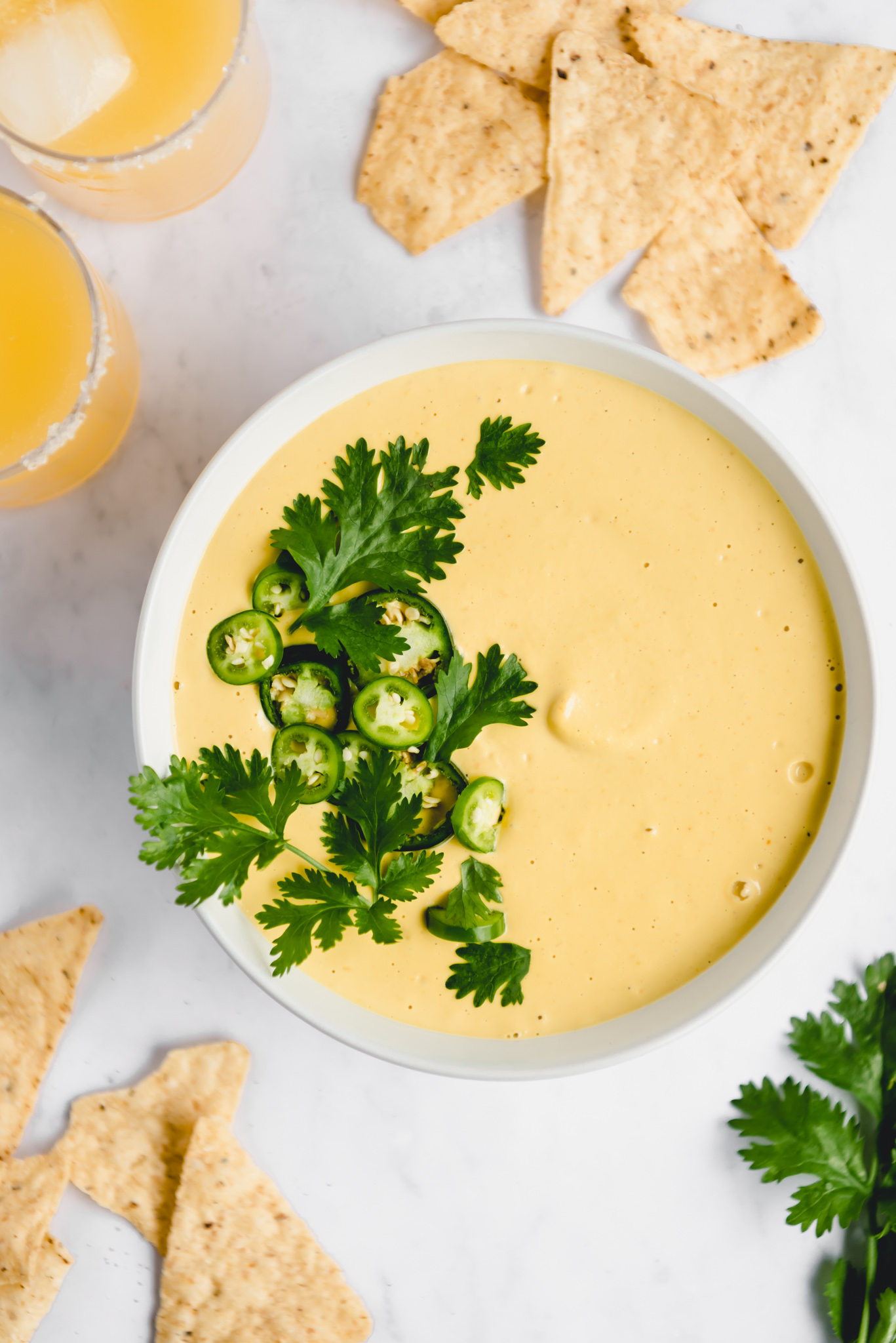 vegan nacho cheese dip with chips and margaritas on white background