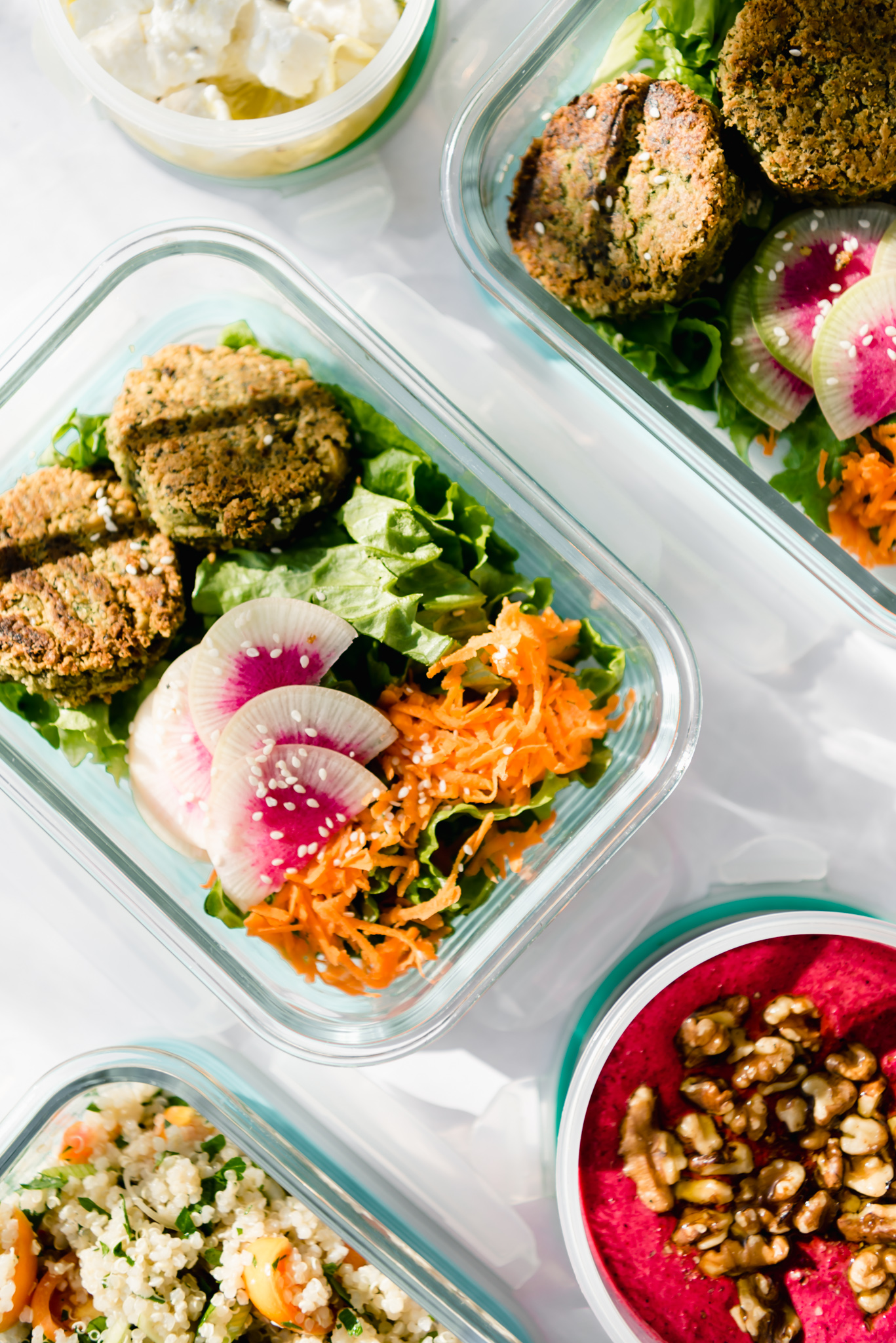 two falafel salad in glass tupperware meal prepped with dips